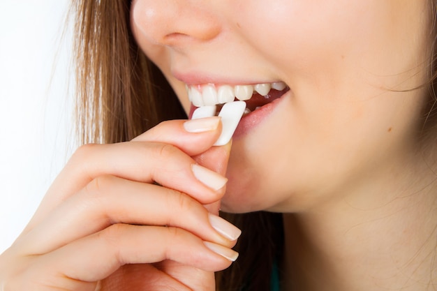 Jeune charmante femme souriante met dans la bouche du chewing-gum