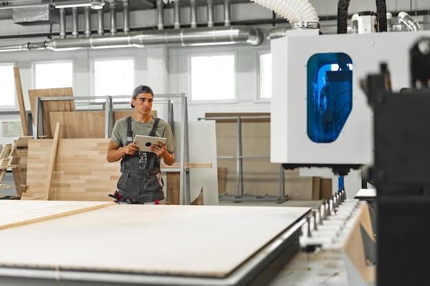 Jeune charpentier opérant une machine pour la transformation du bois dans une usine de meubles en gros plan