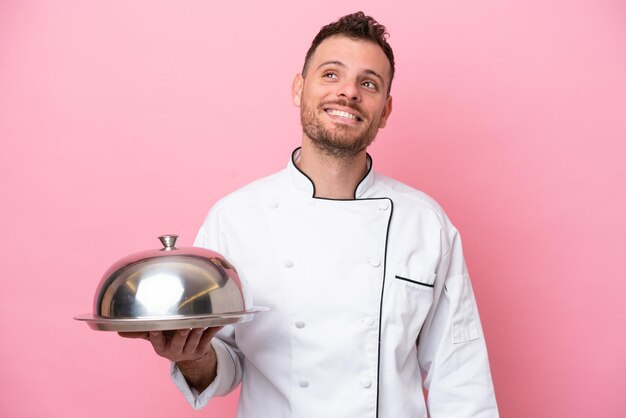 Jeune chef brésilien avec plateau isolé sur fond rose pensant à une idée tout en levant les yeux