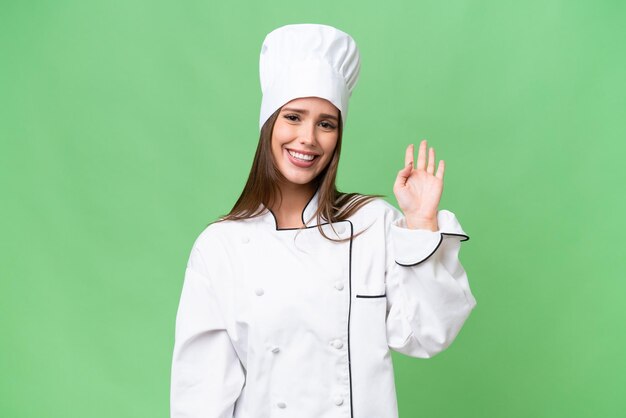 Jeune chef caucasien femme sur fond isolé saluant avec la main avec une expression heureuse