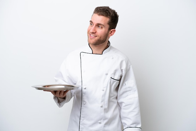 Jeune chef caucasien avec plateau isolé sur fond blanc regardant sur le côté et souriant