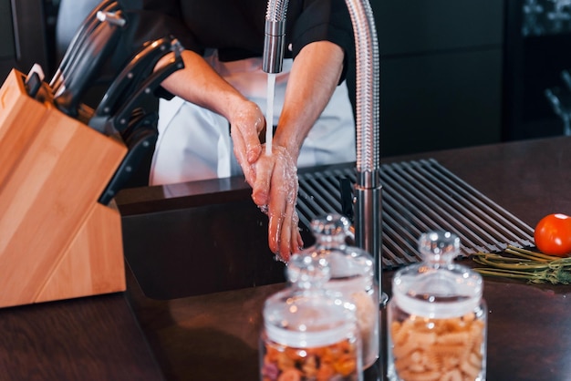 Jeune chef cuisinier professionnel en uniforme se lavant les mains dans la cuisine