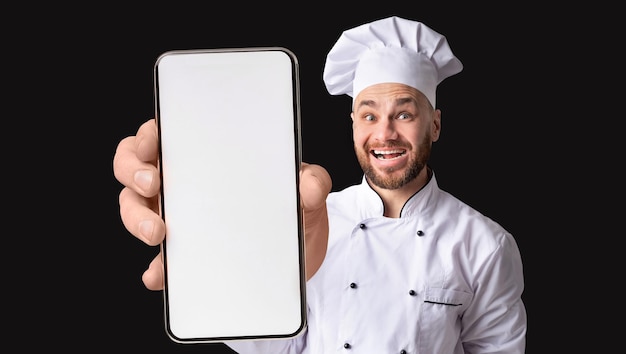 Jeune chef drôle tenant un smartphone démontrant avec un écran vide à la caméra