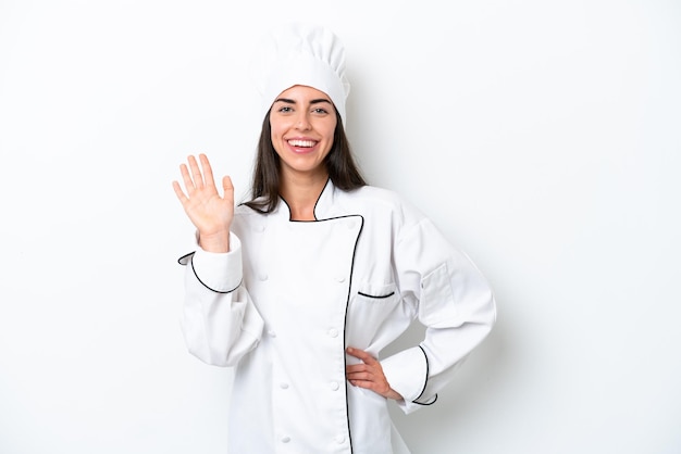 Jeune chef femme sur fond blanc saluant avec la main avec une expression heureuse