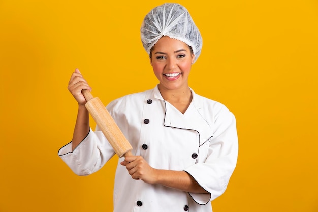 Jeune chef femme en uniforme blanc tient un rouleau à pâtisserie sur fond jaune