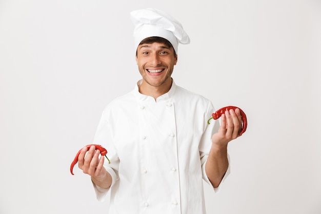 Jeune chef homme debout isolé sur mur blanc tenant le piment.