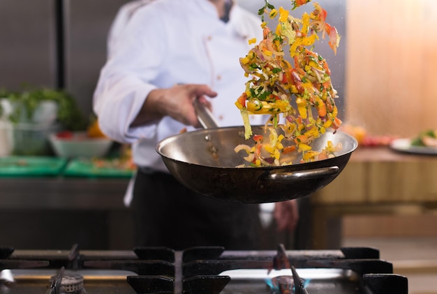 Jeune chef masculin renversant des légumes dans un wok dans une cuisine commerciale