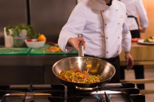 Jeune chef masculin renversant des légumes dans un wok dans une cuisine commerciale