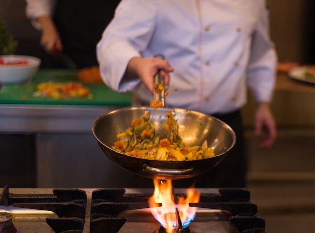 Jeune chef masculin renversant des légumes dans un wok dans une cuisine commerciale