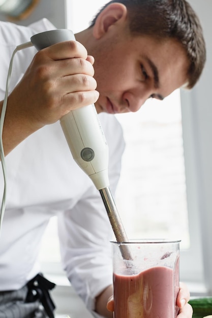 Jeune chef masculin en uniforme faisant un smoothie frais avec un mixeur