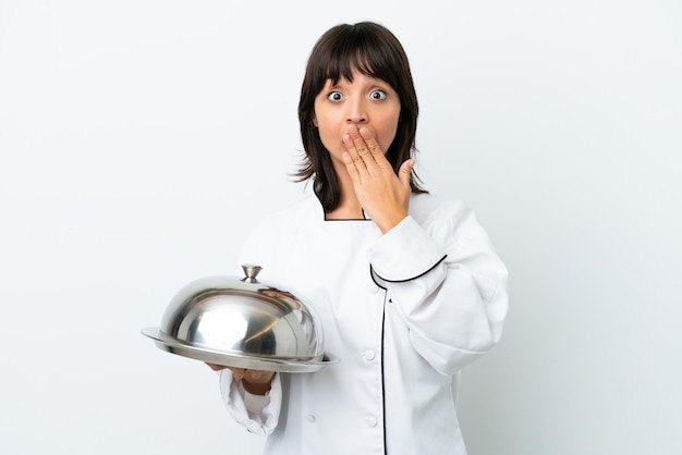 Jeune chef avec plateau isolé sur fond blanc heureux et souriant couvrant la bouche avec la main