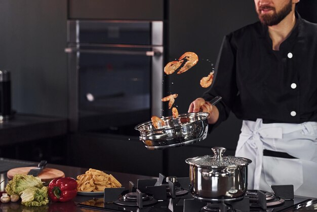 Jeune chef professionnel cuisinier en uniforme faisant frire des aliments dans la cuisine