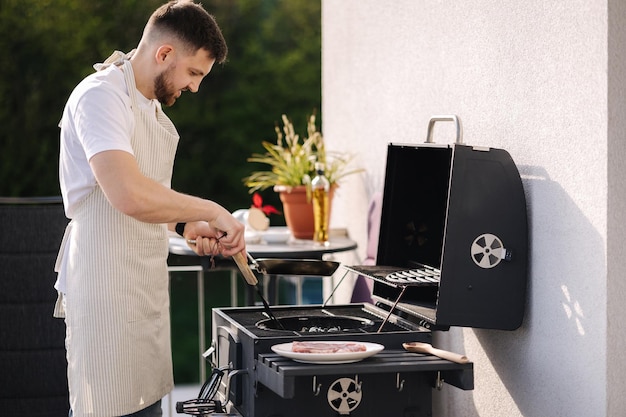 Jeune chef en tablier se préparant à faire cuire un steak sur un barbecue vue latérale d'un homme préparant des aliments pour la vidéo
