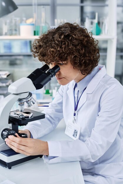 Jeune chimiste ou virologue en blouse de laboratoire regardant au microscope en laboratoire