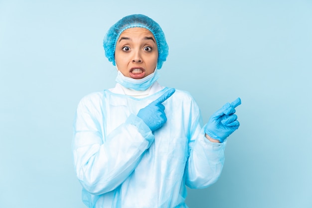 Jeune chirurgien femme indienne en uniforme bleu effrayé et pointant vers le côté