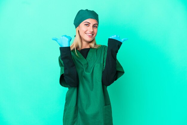 Jeune chirurgien femme uruguayenne en uniforme vert isolé sur fond bleu avec le geste du pouce levé et souriant