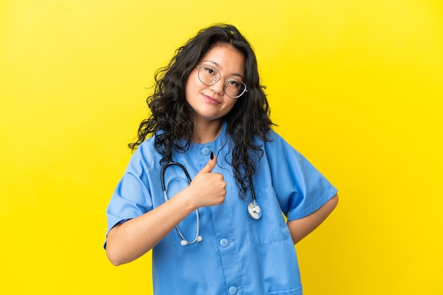 Jeune chirurgien médecin femme asiatique isolée sur fond jaune donnant un geste du pouce vers le haut