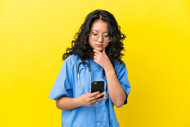 Jeune chirurgien médecin femme asiatique isolée sur fond jaune pensant et envoyant un message