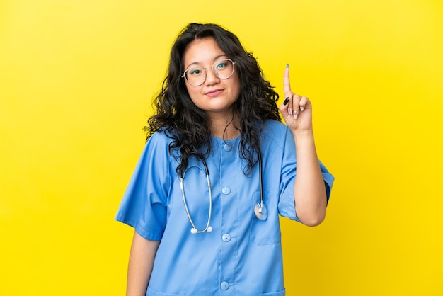 Jeune chirurgien médecin femme asiatique isolée sur fond jaune pointant avec l'index une excellente idée