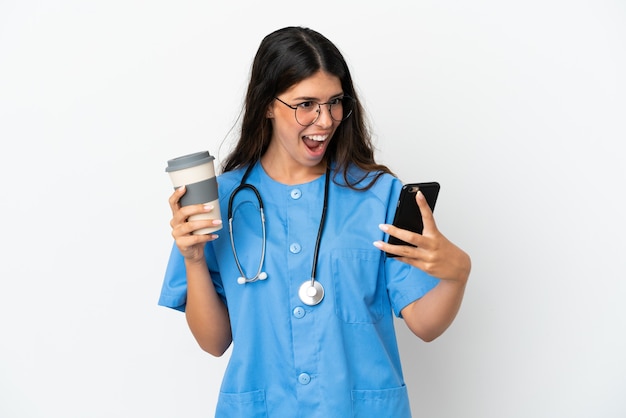 Jeune chirurgien médecin femme caucasienne isolée sur fond blanc tenant du café à emporter et un mobile