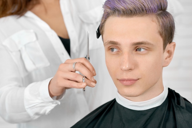 Jeune client avec des cheveux lilas toniques assis coiffure blanche.