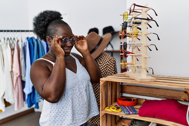 Jeune cliente afro-américaine choisissant des lunettes de soleil dans un magasin de vêtements