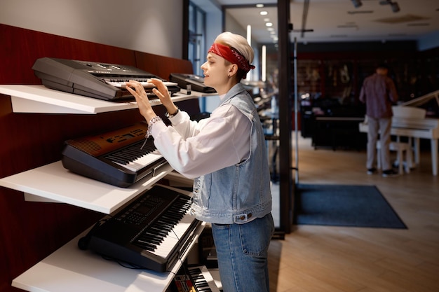 Une jeune cliente choisissant un synthétiseur électrique dans un magasin de musique assortiment d'instruments de clavier dans un atelier de studio de musique