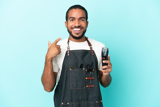 Jeune coiffeur homme latin isolé sur fond bleu donnant un geste du pouce levé