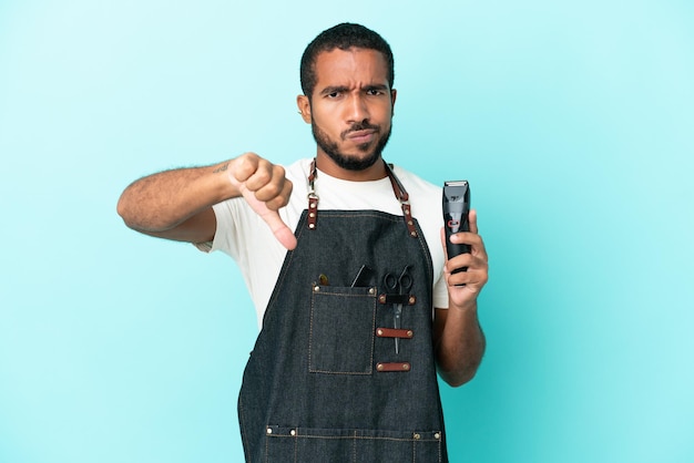 Jeune coiffeur homme latin isolé sur fond bleu montrant le pouce vers le bas avec une expression négative