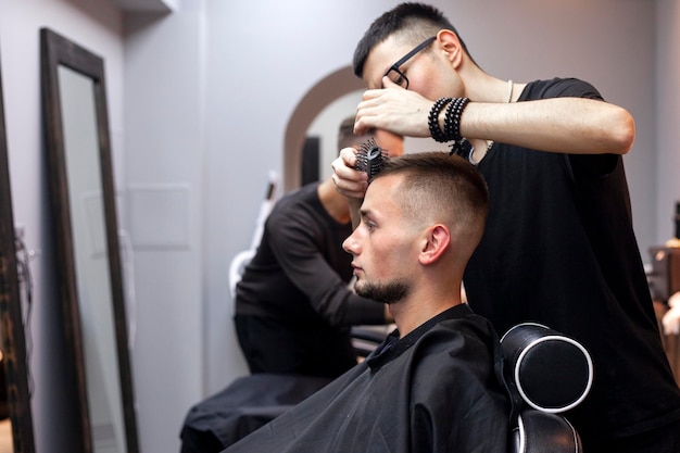 Jeune coiffeur kazakh travaille dans un salon de coiffure beau mec fait la coiffure pour un client