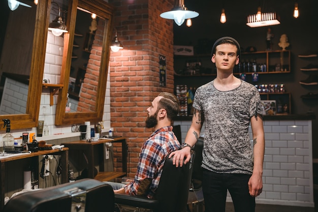 Jeune coiffeur moderne sur son lieu de travail avec client dans un salon de coiffure