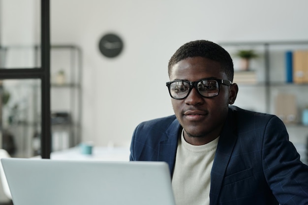 Jeune col blanc sérieux à lunettes assis devant un ordinateur portable