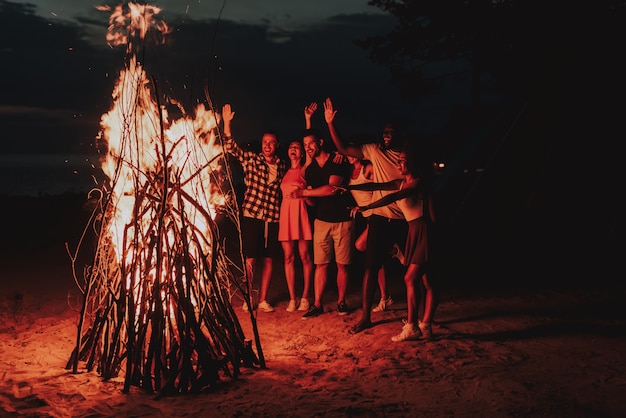 Jeune compagnie dansant autour du feu de joie sur la plage.