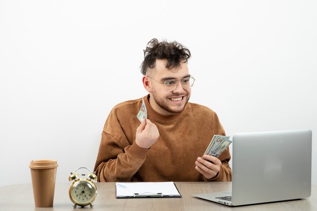 Jeune comptable masculin assis à son bureau et montrant de l'argent.