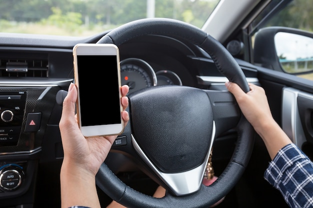 Jeune conductrice à l&#39;aide d&#39;un smartphone à écran tactile et main tenant le volant dans une voiture.