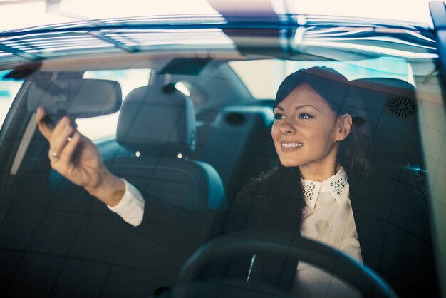 Jeune conductrice ajuste son rétroviseur dans la voiture.