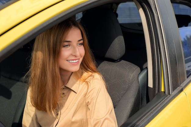 Jeune conductrice souriante regardant par la fenêtre de sa voiture jaune alors qu'elle était assise sur le siège du conducteur