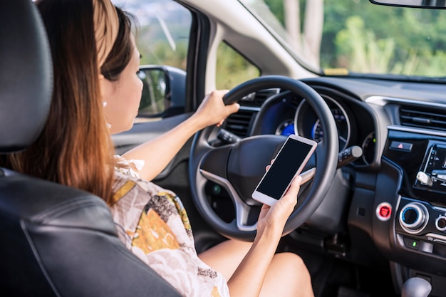 Jeune conductrice tenant un téléphone intelligent avec copie espace pendant la conduite, indiquant la négligence