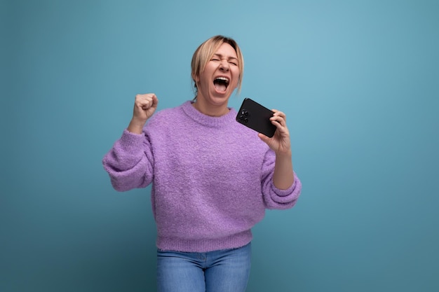 Jeune consultante blonde énergique en sweat à capuche violet tenant un smartphone avec maquette et chantant