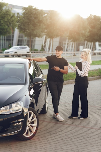 Une jeune consultante blonde montre au client la voiture à l'extérieur. Un homme achète une voiture. Testez une nouvelle voiture.