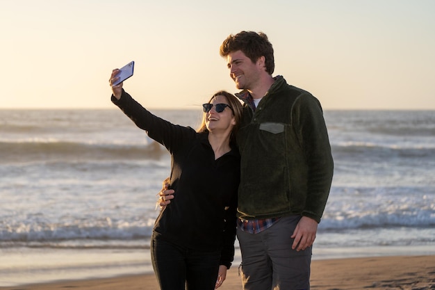 Jeune copule prenant des selfies sur la plage au coucher du soleil