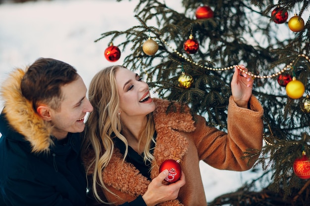 Un jeune couple adulte décore l'arbre de Noël dans la forêt de sapins en bois du parc d'hiver. Concept de célébration de fête de vacances de pin du nouvel an.