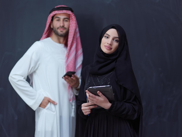 jeune couple d'affaires musulman homme arabe avec une femme en robe hijab à la mode à l'aide d'un téléphone portable et d'une tablette devant un tableau noir représentant la technologie de la mode islamique moderne et le rama