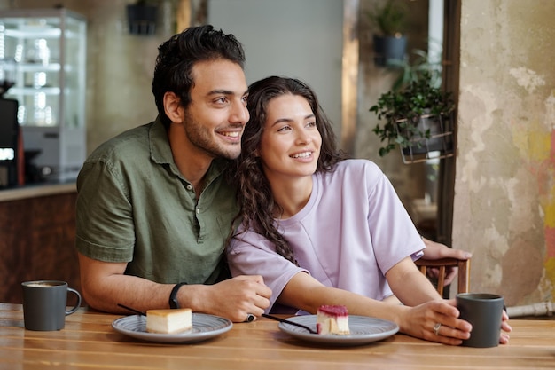 Jeune couple affectueux regardant par la fenêtre tout en étant assis à table dans un café