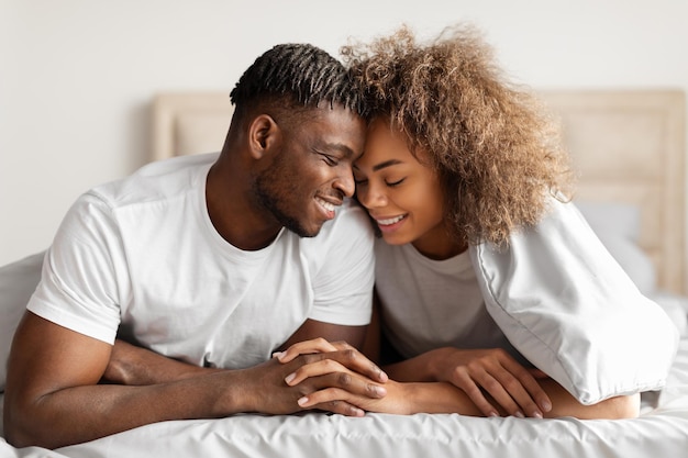 Un jeune couple africain se tenant par la main et se touchant le front dans le lit.