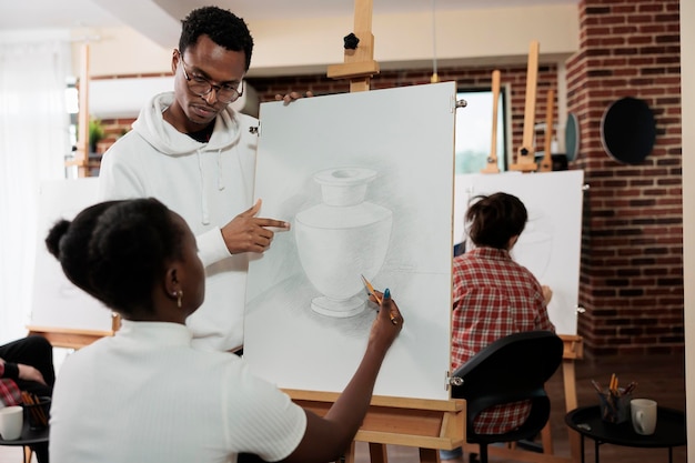 Photo jeune couple afro-américain assistant ensemble à un cours d'art en groupe, essayant de nouvelles choses pendant son temps libre, un enseignant aidant un élève pendant une leçon de dessin dans un studio de création. passe-temps artistique