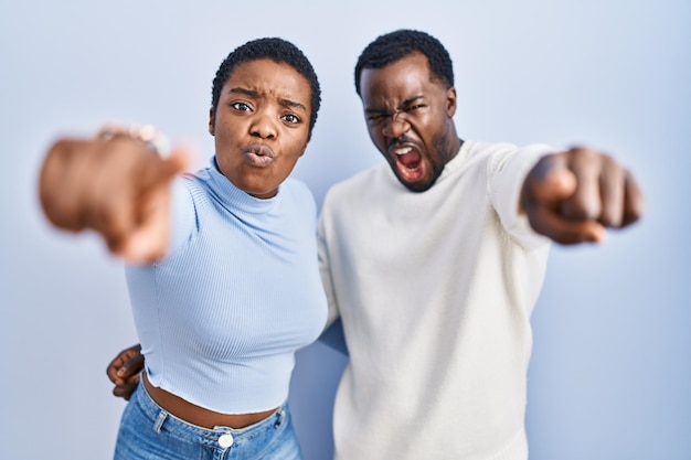 Photo jeune couple afro-américain debout sur fond bleu pointant mécontent et frustré vers la caméra, en colère et furieux contre vous