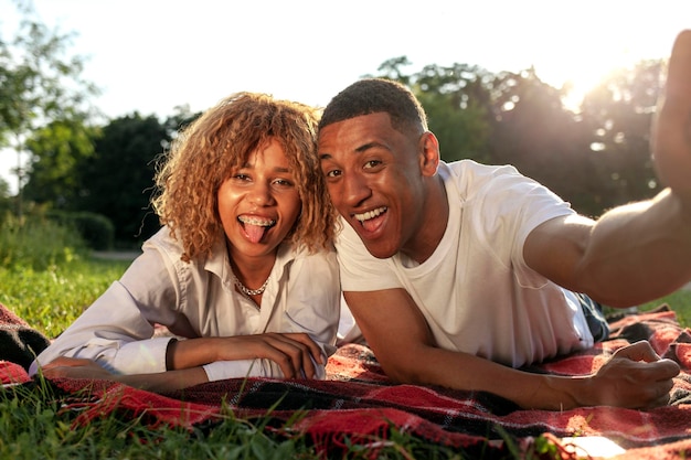 Un jeune couple afro-américain est allongé dans le parc en été sur l'herbe et prend un selfie.