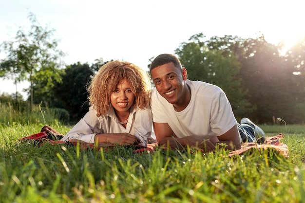 Un jeune couple afro-américain est allongé dans le parc en été sur l'herbe et sourit.