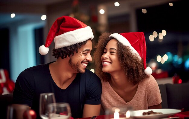 Un jeune couple afro-américain portant des chapeaux de Père Noël riant et profitant du dîner de Noël dans leur maison confortable avec des lumières bokeh en arrière-plan concept de festivités de Noël et du Nouvel An